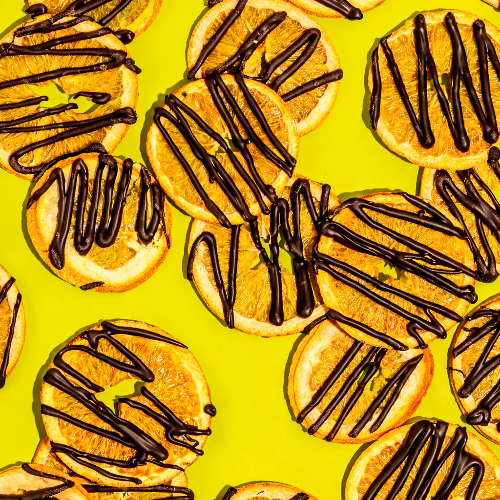 Dark Chocolate Drizzled Orange Chips on a vibrant yellow background, showcasing a tasty balance of flavors.